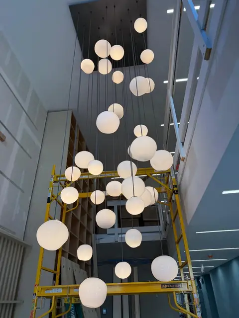Lámparas de globos en cascada en un atrio de tres pisos, durante la instalación